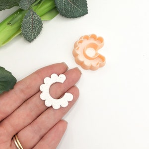 Flower-shaped scalloped clay cutter tool held in hand, light-colored