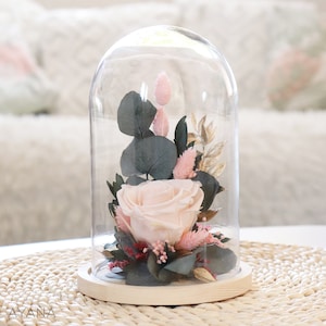 Decorative glass bell with preserved pink rose, dark leaves, and dried beige blooms on base