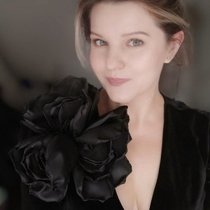 Large black fabric flower brooch pin with layered petals on a dark garment