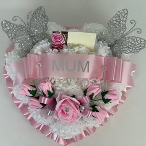Heart-shaped artificial flower wreath with pink and white blooms, ribbons, and glitter butterflies
