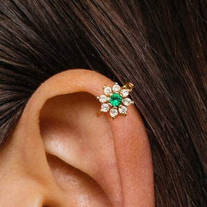 Gold flower hoop earring with emerald-green center and clear stones on upper ear