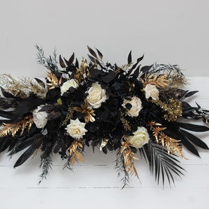 Boho faux floral arch centerpiece with black and ivory blooms, gold accents, and leafy greenery.