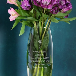 Clear glass bullet vase with engraved note, holding pink and purple roses and greenery