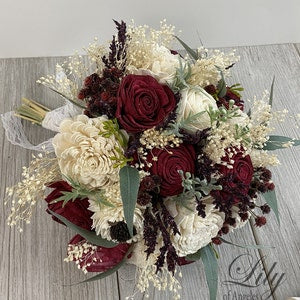 Rustic bridal bouquet with burgundy and ivory flowers, lace ribbon, and greenery