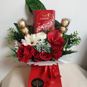 Red and cream silk flower gift hamper with roses, greenery, ribbon, and chocolate decor