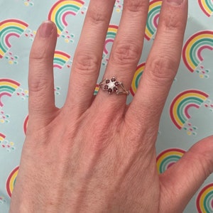 Silver-tone flower cluster ring with opal and red garnet-style gemstones, openwork band
