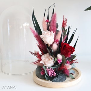 Dried rose and pink flower arrangement under clear glass dome on round base