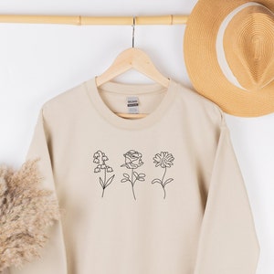 Light cream sweatshirt with minimalist line-art birth flower graphic on chest