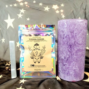 Herbal blend pouch (TUNDRA CLOUDS) with deer graphic, beside a purple pillar candle
