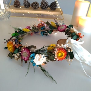 Colorful dried flower crown wreath with small blooms and long white satin ribbons