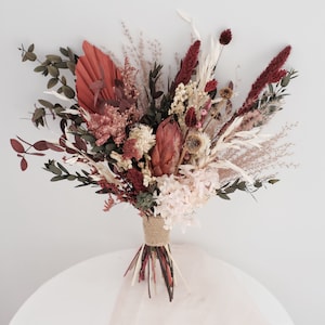 Rust and burgundy dried bridal bouquet with white blooms, long grasses, wrapped stems