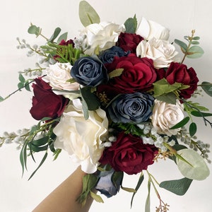 Silk wedding bouquet with ivory, navy, and burgundy roses and eucalyptus leaves, held in hand