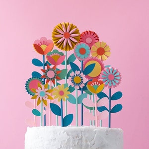 Colorful paper flower cake toppers in pink, yellow, teal on a white cake
