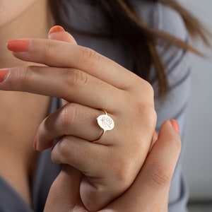 Gold-tone floral signet ring with engraved blossom on finger