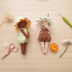Crochet amigurumi flower sprite dolls, one brown and green, one brown and gray, flat lay