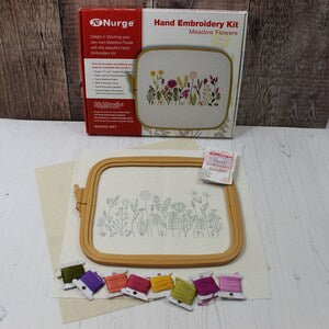 Hand embroidery kit with tan plastic hoop, printed meadow flower fabric, and colored threads