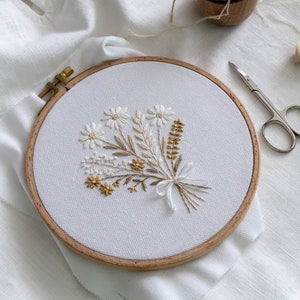 Floral bouquet embroidery in wooden hoop on light fabric, delicate gold thread