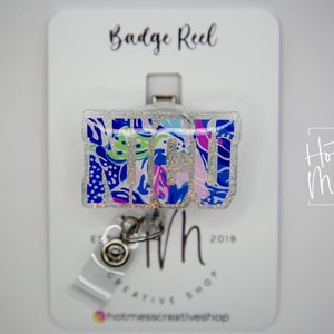Glitter floral badge reel with retractable metal clip, blue and purple design