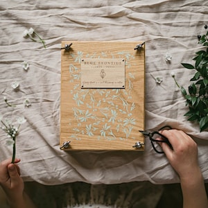 Large wooden flower press with botanical cover and corner clamps, holding dried leaves