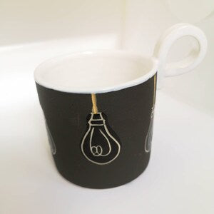 Ceramic lightbulb mug with black body and white interior, lightbulb graphic
