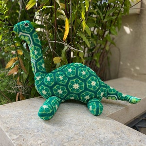 Teal green crocheted dinosaur amigurumi with flower granny square pattern
