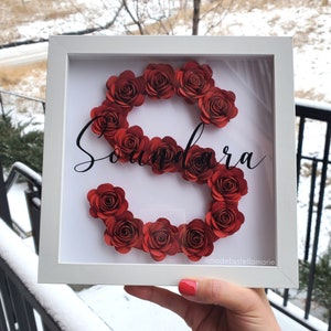 White shadow box with red paper rose wreath and cursive monogram