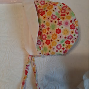 Baby bonnet with multicolor floral top and cream fabric sides, with tie strings
