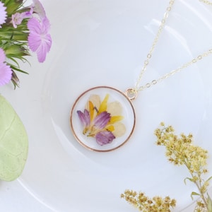 Pressed flower resin necklace with circular pendant, gold chain, dried blooms inside.
