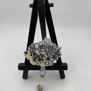 Silver flower badge reel with black ribbon and retractable clip on stand