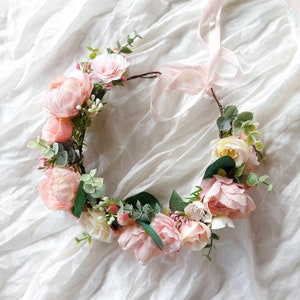 Pink flower crown with pastel blooms and green leaves on a ribbon band