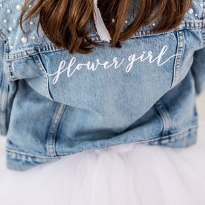 Light blue denim jacket with white 'flower girl' script on chest