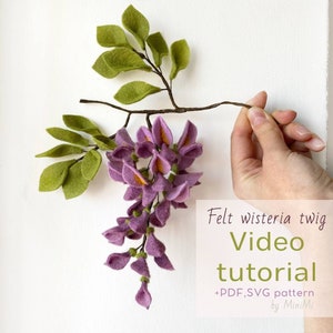 Felt wisteria flower twig with purple blossoms and green leaves, shown held by hand