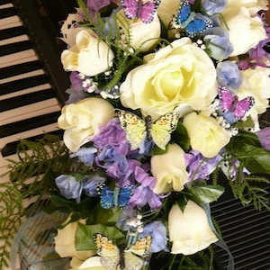 Cascade wedding bouquet with ivory roses, purple flowers, and butterfly accents