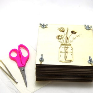 Flower press kit with illustrated paper cover, stacked wooden boards, and corner screws