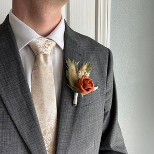 Terracotta rose boutonniere with pale bunny tail on suit lapel