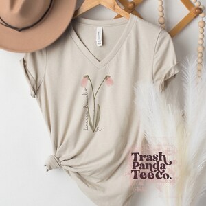 Beige V-neck tee with linnea flower print and 'Trash Panda TeeCo.'