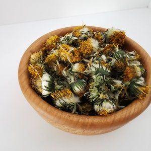 Dried dandelion flowers, yellow blossoms with green leaves in a wooden bowl