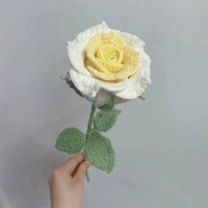 Crocheted rose flower with cream center, white petals, and green leaves