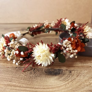 Dried flower crown with burnt orange, red and white blooms and green leaves