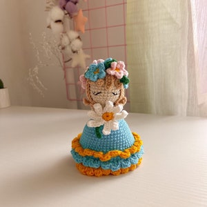 Crochet amigurumi bouquet doll with blue layered dress and flower hat, holding bouquet