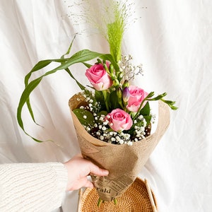 Fresh flower bouquet with pink roses in brown kraft paper wrap, held by a hand
