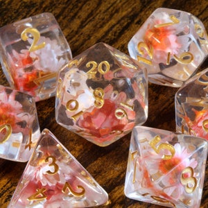 Translucent resin dice set with pink flower inclusions and gold numbers, D20 and more