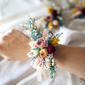 Dried flowers wrist corsage with pink roses, blue and yellow blooms, worn on wrist