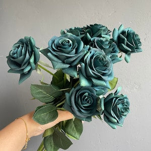 Teal green faux rose bouquet with multiple blooms and green leaves, hand holding