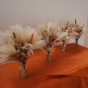Terracotta-toned dried flower bouquet with feathery beige blooms in glass vases