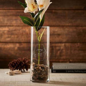 Clear glass table vase with engraved text, holding white flowers and small filler stones
