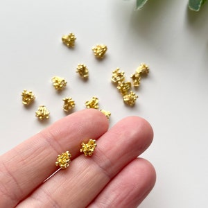 Brass flower-shaped charm centers in gold tone, small clustered pieces held in hand