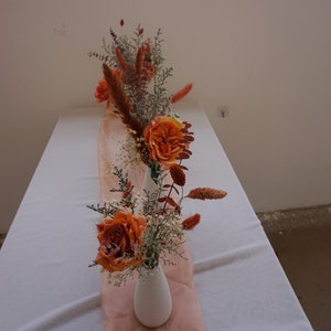 Dried floral arrangement in a small white vase with terracotta orange flowers