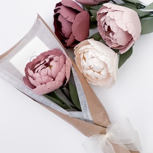Stemmed paper peony bouquet with pink and white flowers, green leaves, wrapped in kraft paper.