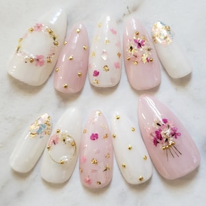 Press-on nails set with white and pink tips, dried flowers, and gold accents